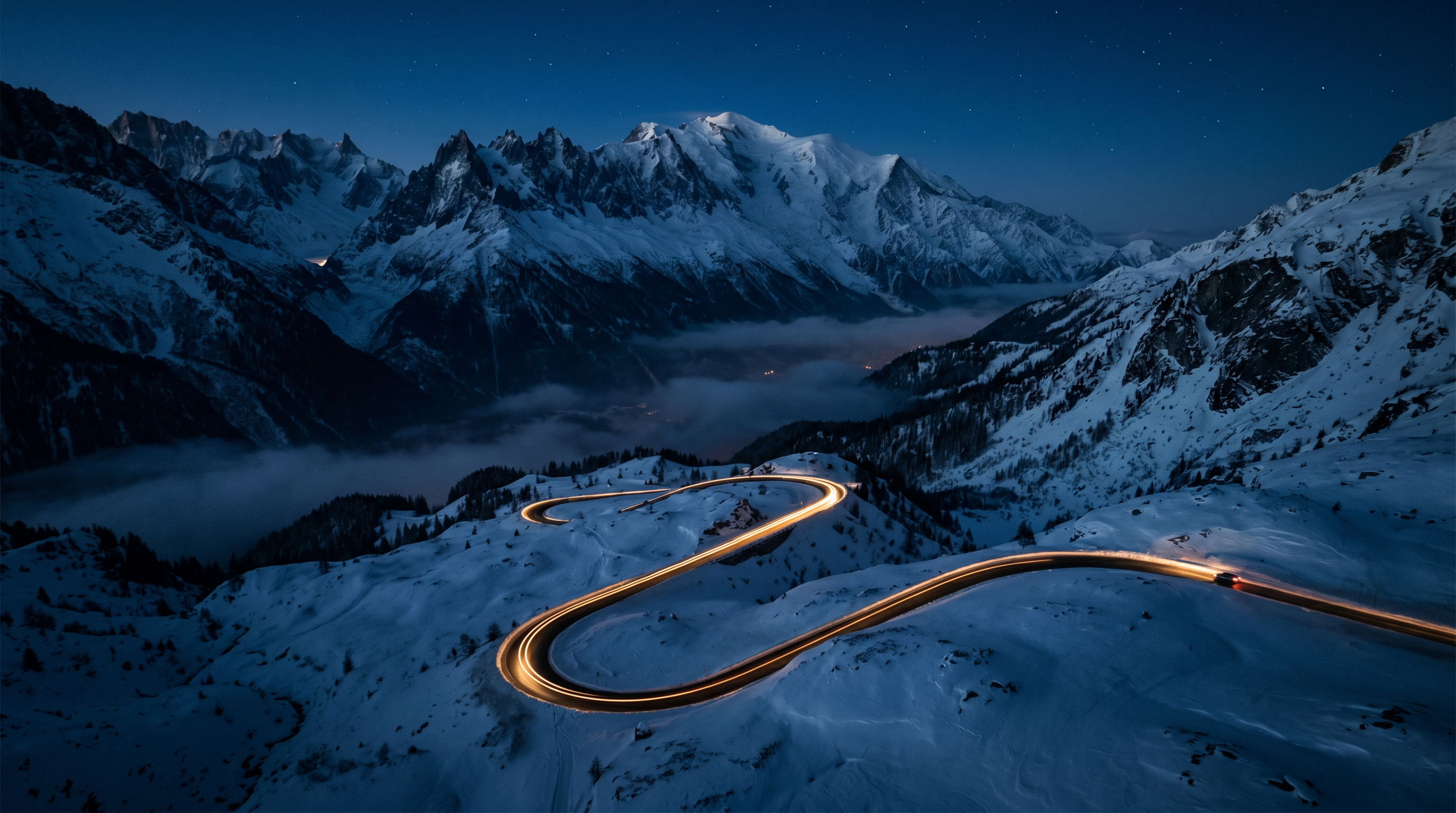 Winding mountain road at night beneath snow-capped peaks